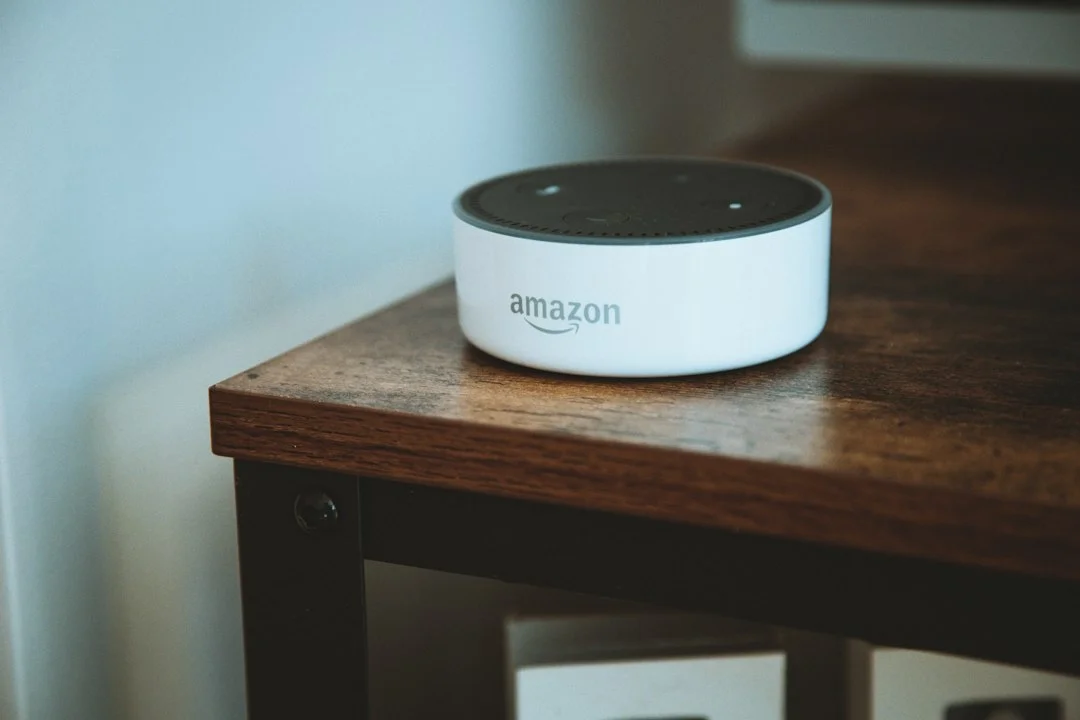A reference photo of a white Amazon Echo Dot smart speaker placed on a wooden table. The Alexa Tablet body or the Alexa+ screen is not shown.