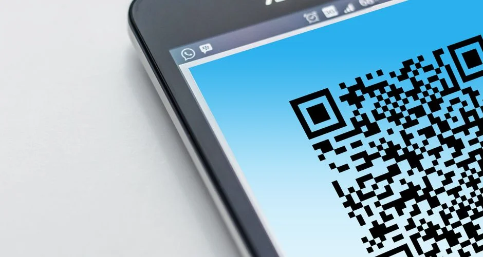 기기 화면에 파란 배경의 QR 코드가 크게 표시된 근접 사진. 화면 상단에 메신저 앱 아이콘이 보이나 로그인 절차 자체는 식별되지 않는 중립적 참고 사진