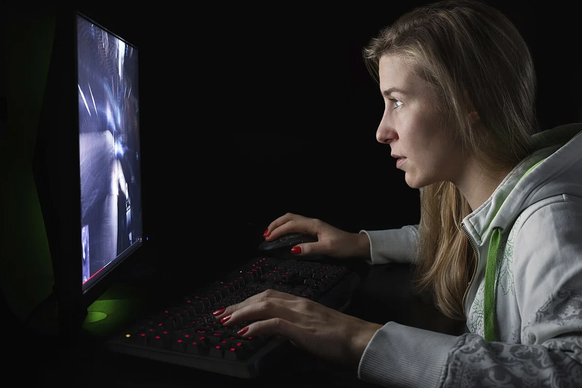 A person sitting in front of a monitor in a dark room, playing a game with a keyboard and mouse. A neutral reference photo related to the final section covering the player's perspective while no release date has been set; it is not a gameplay scene of the specific game (Haunted Chocolatier).