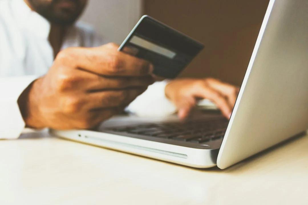 A person holding a credit card while typing on a laptop at a desk. Generic online shopping scene; it does not show the actual Amazon listing or a verified iPad Mini sale price.