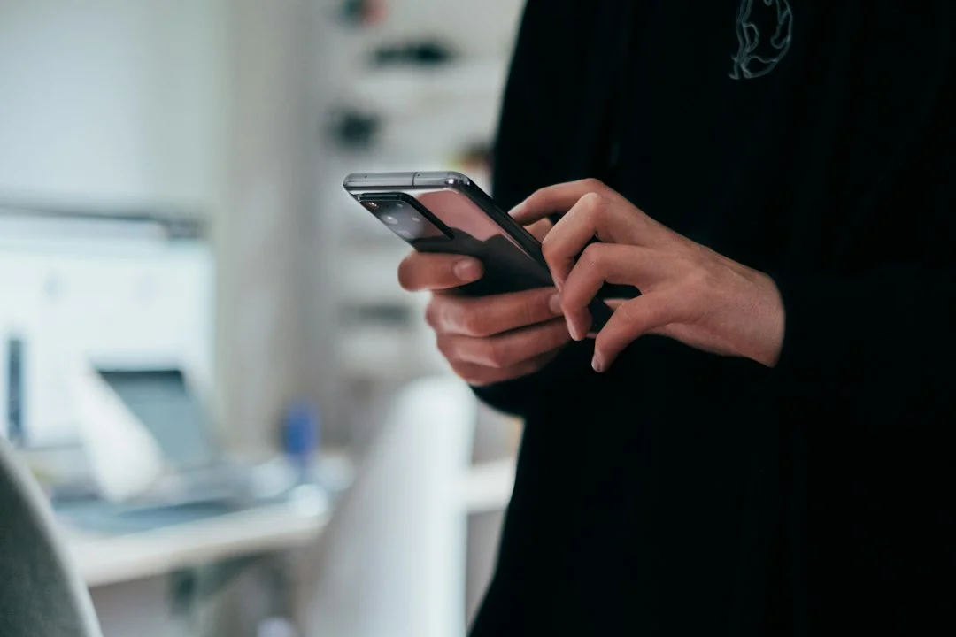 Reference photo of a person indoors holding a smartphone with both hands and touching the screen. It does not show a foldable screen's Split View or Duo Preview features, but is a generic scene on the topic of app usage.